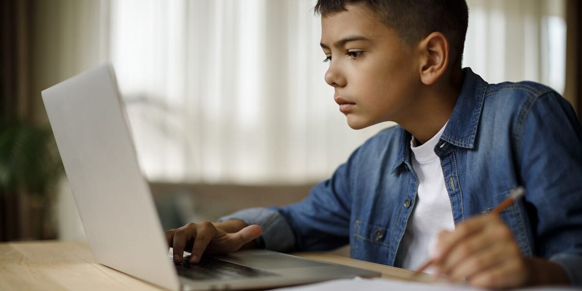 Teenage boy using laptop for homework kid on his computer learning virtually and taking notes