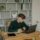 A-Male-Student-in-Green-Long-Sleeves-Using-a-Laptop-on-a-Wooden-Desk-scaled