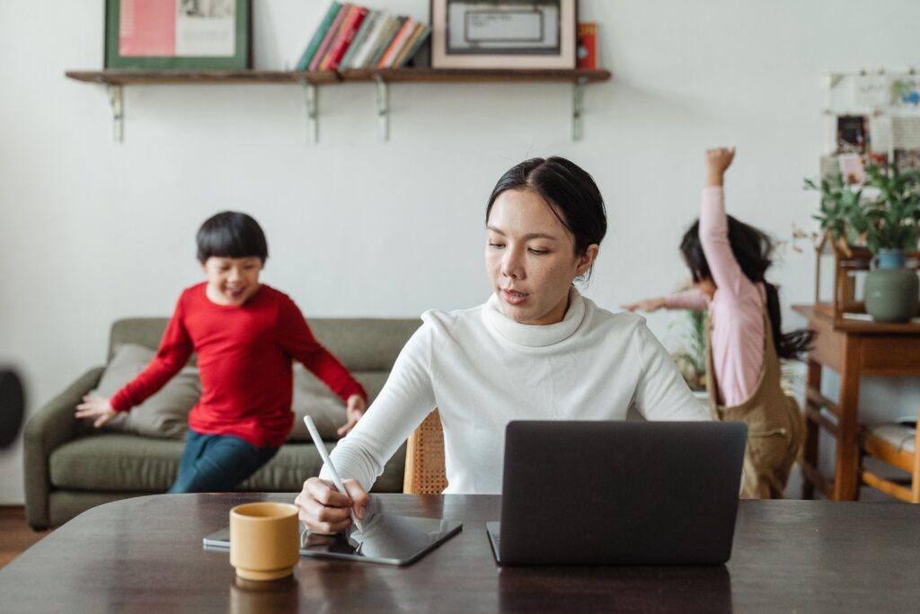 mother working on a laptop at home while her children play
