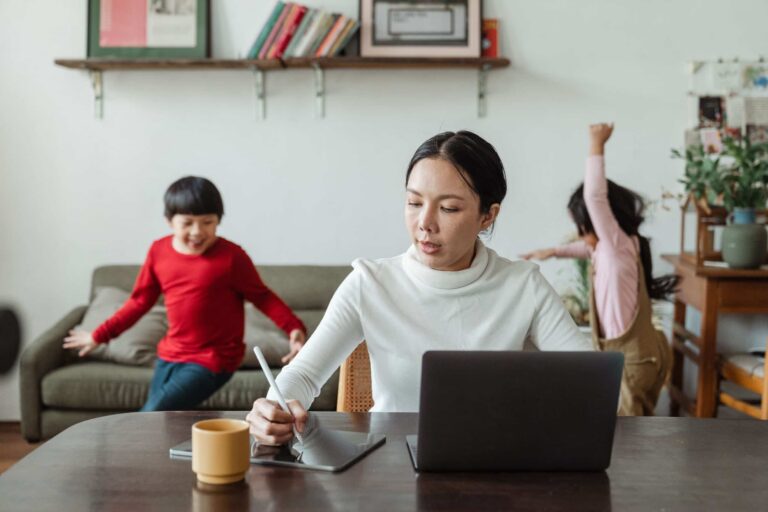 mother working on a laptop at home while her children play